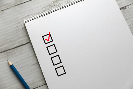 Selective focus of a pen and book with blank checklist on a white wooden background.