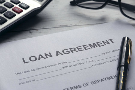 Selective focus of calculator,glasses,pen and Loan Agreement letter on white wooden background.の写真素材