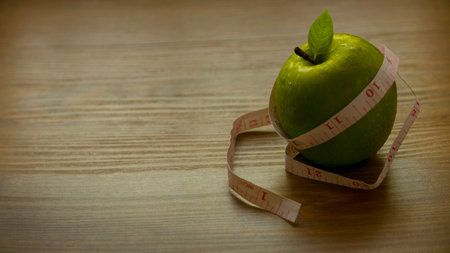 Diet concept. Green apple with measuring tape on wooden background with copy space.の写真素材