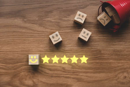 Top view of a fallen red bucket fill with icon of face expression of rating on wooden cube. Customer...