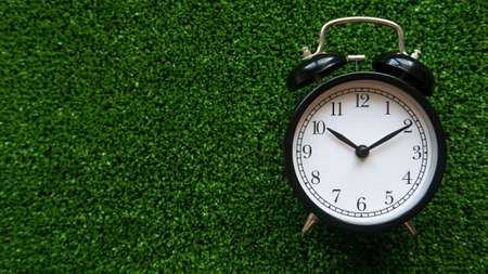 A vintage alarm clock on green grass background with copy space.