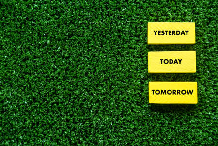 A yellow wooden cube written with text of Yesterday, Today and Tomorrow on a green grass background with copy space.の写真素材