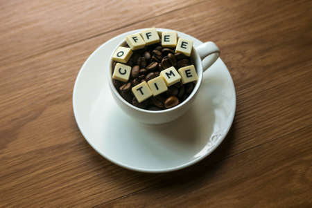 Selective focus of a cup of coffee beans with an alphabet with text of Coffee Time on wooden background.の写真素材