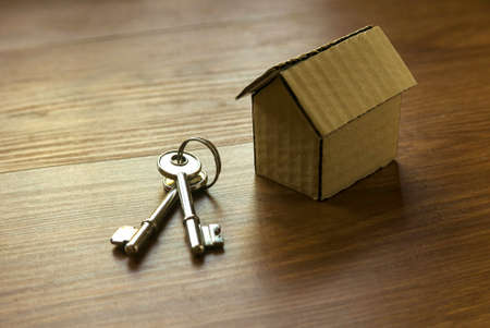 Close up of house model and keys on wooden background.
