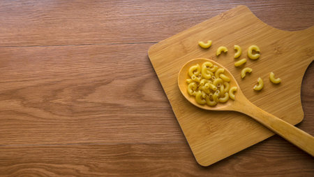Raw and uncooked elbow macaroni on wooden wooden spoon on wooden background with copy space.の写真素材
