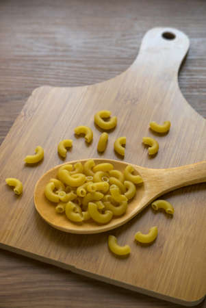 Raw and uncooked elbow macaroni on wooden wooden spoon.