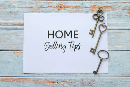 Top view of keys and paper written with Home Selling Tips on wooden background.