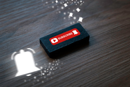 Wooden button with subscribe note and notification bell icon on wooden background. Motion blur of white notification bell. Concept of social media and digital online.の写真素材