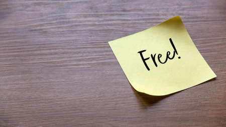 A yellow memo sticky note written with FREE on a wooden background with copy space.の写真素材