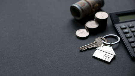 House key together with calculator, money and a stack of coins on black background with copy space.の写真素材