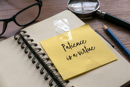 Selective focus of glasses, pencil, magnifying glass, notebook and yellow paper written with Patience is a virtue.の写真素材