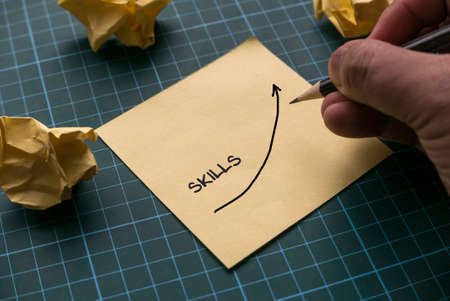 A hand drawing a graph of skills on a yellow memo paper note on a green craft mat.の写真素材