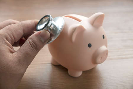 A hand holding stethoscope to a piggy bank.の写真素材