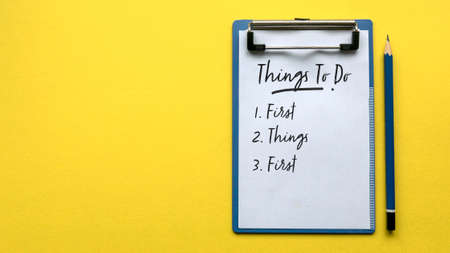Top view of a pencil and a clipboard with paper written with Things To Do and a number with sentence First Things First on a yellow background with copy space.の写真素材