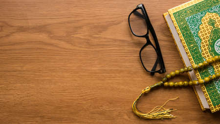 Top view of glasses, rosary beads and Quran on wooden background with copy space.