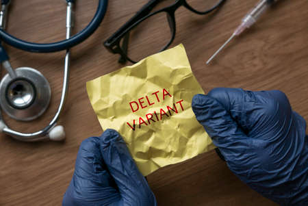 A hand wearing blue glove opening a crumpled yellow memo note written with Delta Variant.の写真素材