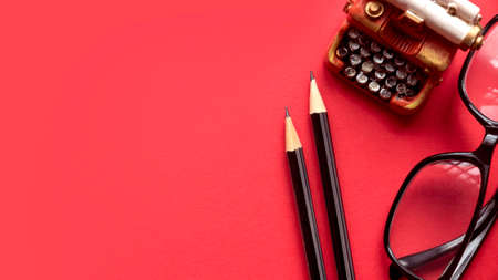 Pencil, glasses and miniature typewriter on red background with copy space.の写真素材