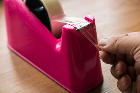Selective focus of hand pulling a transparent tape from a tape dispenser.の写真素材