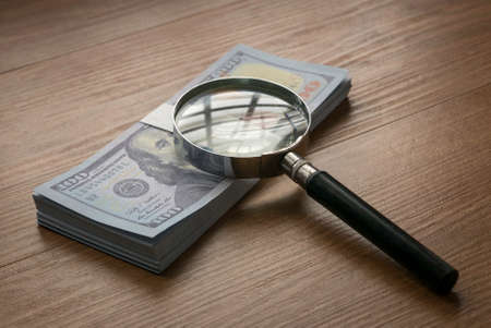 Selective focus of magnifying glass and money on a wooden background.の写真素材