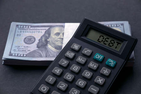 Selective focus of money and calculator with word DEBT on a black background.の写真素材