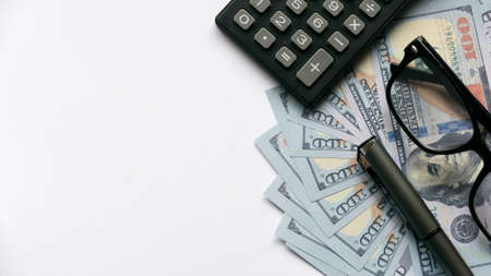 A calculator, pen and glasses on a dollar money or bank notes on white background with copy space.の写真素材