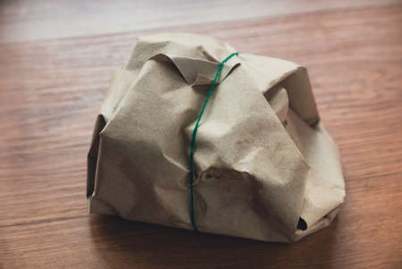 Rice with several side dish wrap with brown oil paper and rubber band on wooden background.