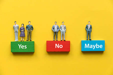 Miniature people standing on wooden block represent an option of YES,NO and MAYBE.