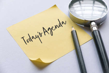 Pencil, magnifying glass and yellow memo note written with Today's Agenda on white background.