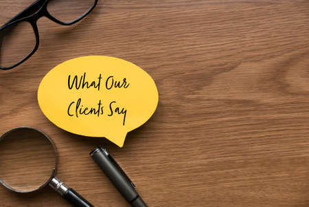 Top view of magnifying glass, glasses, pen and yellow speech bubble written with What Our Clients...