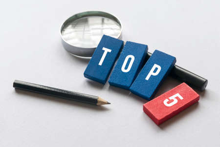 Pencil, magnifying glass and wooden block written with Top 5 on white background.