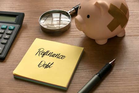 Selective focus of calculator, magnifying glass, piggy bank, pen and memo note written with Refinance Debt on wooden background.の写真素材