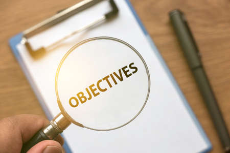 A hand magnifying a words of Objectives from a white paper using magnifying glass.の写真素材