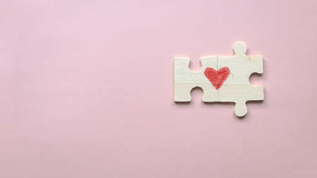Top view of two pieces of a puzzle forming a heart on a pink background with copy space. Love concept.の写真素材