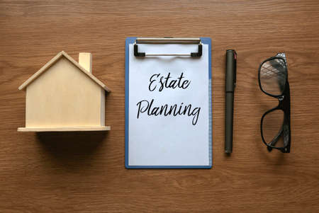 Top view of house model, glasses, pen and clipboard with paper written with Estate Planning on wooden background.の写真素材