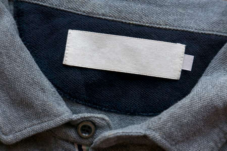 Blank white laundry care clothes label on grey fabric texture background.