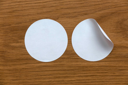 Blank white round stickers straightened and with folded corner on wooden background.の写真素材