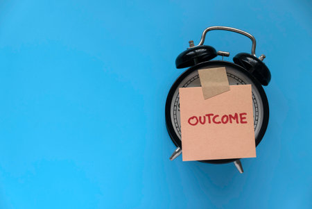Outcome concept. A note written with outcome on alarm clock.の写真素材