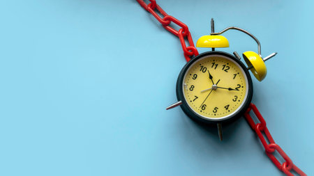 Concept of time management, deadline, work pressure. Alarm clock attached to a red chain. Blue...