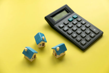 Concept of home loan mortgage, refinance, interest rate. Saving for house.Miniature house with calculator over yellow background.の写真素材