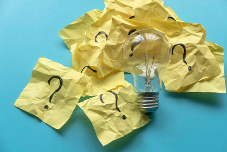 Light bulb with a questions symbol written on a yellow paper over a blue background.の写真素材