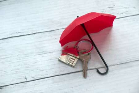 Concept of renters home insurance or mortgage protection. House key under a red umbrella.の写真素材