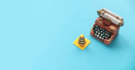 Fixing, maintenance and under construction concept.  Miniature typewriter and traffic cones on blue background.の写真素材