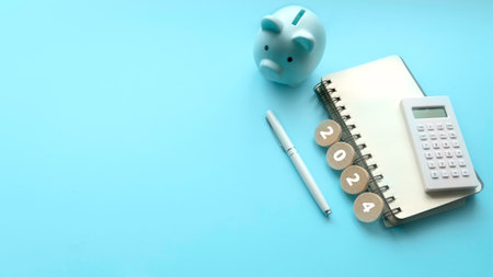 Saving goal for new year. Financial Planning for 2024. Piggybank , notebook and calculator on a blue...