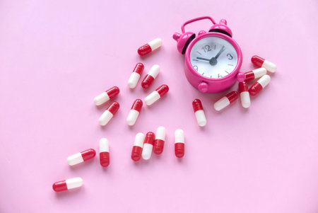 Reminder to take medicine on time, pharmacy, supplements or vitamins. Alarm clock with pills on pink...