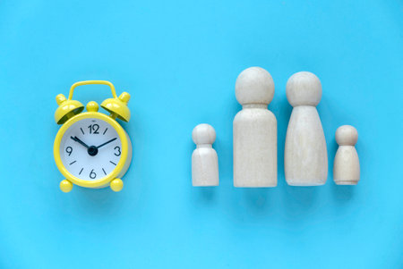 Quality time spent with family. Alarm clock with wooden people represent a parent and children.の写真素材