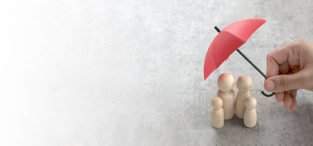 Hand Holding Umbrella Over Wooden Miniature Family Representing Protection, Care, and Security