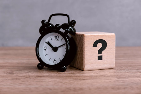 Wooden Cube with Question Mark Symbol with alam clock on wooden table.