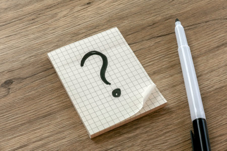 Question Mark on Graph Paper Notepad and pen on Wooden Surfaceの写真素材
