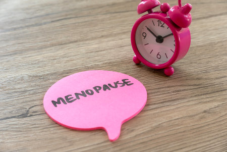Pink Alarm Clock and Speech Bubble with 'Menopause' Text on Wooden Surfaceの写真素材
