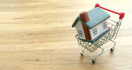 Miniature House in Shopping Cart on Wooden Surface - Real Estate Conceptの写真素材